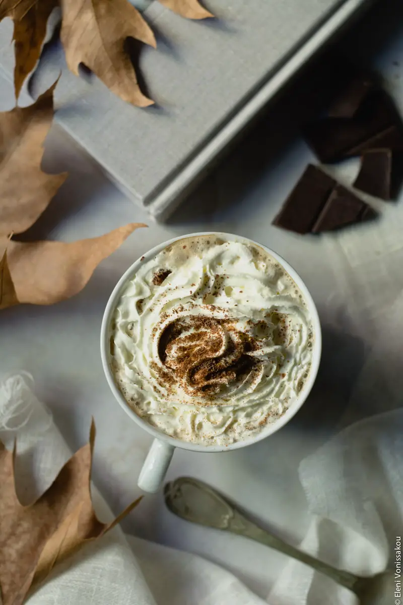 Pumpkin Spice Latte, Καφές Λάτε με Γεύση Κολοκύθας και Μπαχαρικών www.thefoodiecorner.gr 06 Photo description: A closer look at one of the cups of psl with whipped cream and a sprinkling of spices and shaved chocolate. Dry leaves to the left and the handle of an old silver spoon towards the bottom.