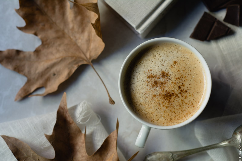 Pumpkin Spice Latte, Καφές Λάτε με Γεύση Κολοκύθας και Μπαχαρικών www.thefoodiecorner.gr 03 Photo description: One cup of psl next to dry autumn leaves, sitting on marble-like surface. A few pieces of dark chocolate visible in the top right corner.