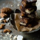 Brownies with Melomakarona and Kourabiedes - Aka Greek Christmas Brownies www.thefoodiecorner.gr A stack of brownies in on flower-shaped pewter-coloured plate stand, with melomakarona and kourabiedes visible where the brownies have been cut. At the side of the stand, some broken up and crumbly melomakarona and kourabiedes. All on a grey metal surface.