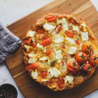 Easy Frittata with Spinach, Cherry Tomatoes and Anthotyro (Ricotta) www.thefoodiecorner.gr Photo description: A round frittata sitting on a wooden chopping board. The top is dotted with pieces of anthotyro and cherry tomatoes. At the side, a few cherry tomatoes on the vine, a linen tea towel and a bunch of thyme. A small bowl of pepper corns just visible at the bottom of the photo.