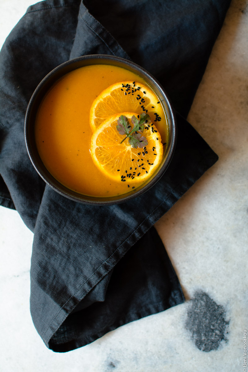 Simple Slow Cooker Carrot and Orange Soup with Turmeric and Cumin www.thefoodiecorner.gr Photo description: One of the bowls sitting on a messily folded black linen napkin. Bowl is towards the top left corner. Garnish as before. In the bottom right corner the marble pattern has a grey smudge on the mostly white surface.