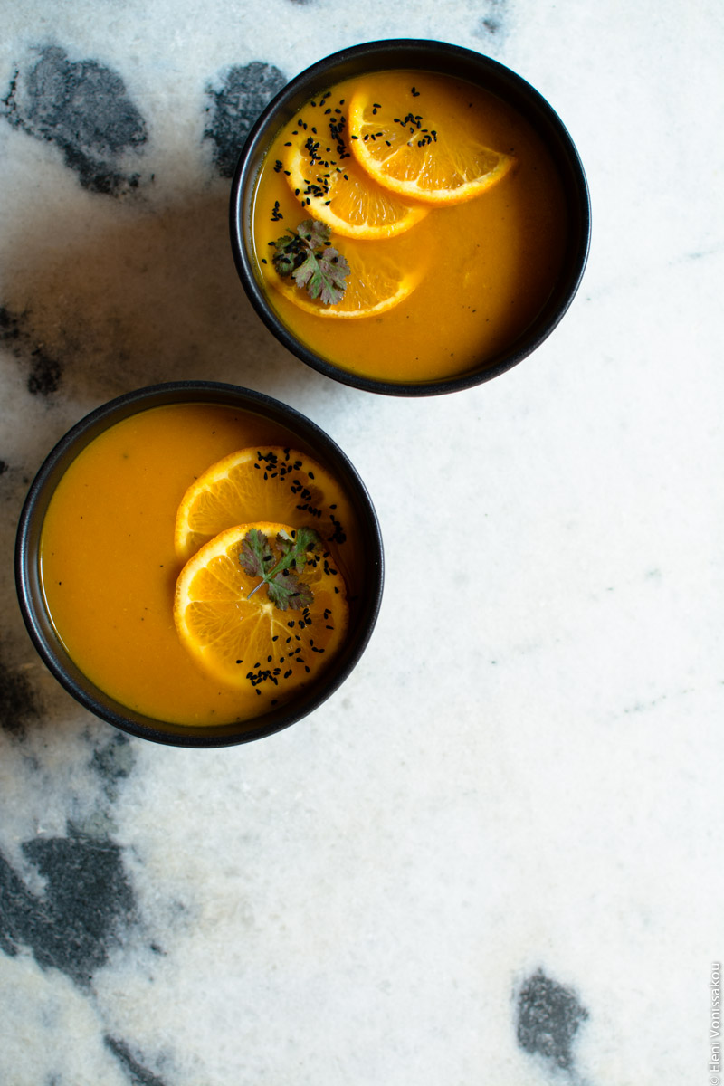 Simple Slow Cooker Carrot and Orange Soup with Turmeric and Cumin www.thefoodiecorner.gr Photo description: The two bowls of soup sitting on the marble surface, one is at the top of the photo, the other just below and to its left. The bottom right corner is all empty white marble space. Garnishes in bowls as before.