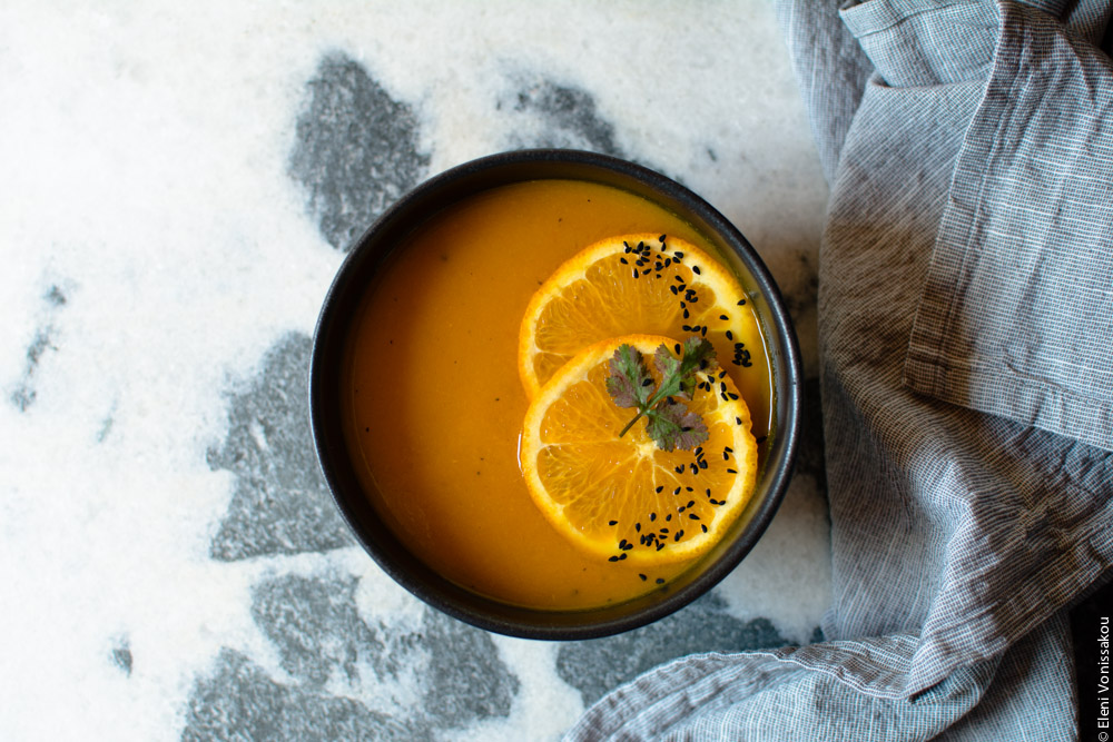 Simple Slow Cooker Carrot and Orange Soup with Turmeric and Cumin www.thefoodiecorner.gr Photo description: Landscape layout photo of one bowl of soup on the marble surface. To its right the bunched up grey linen dish cloth.