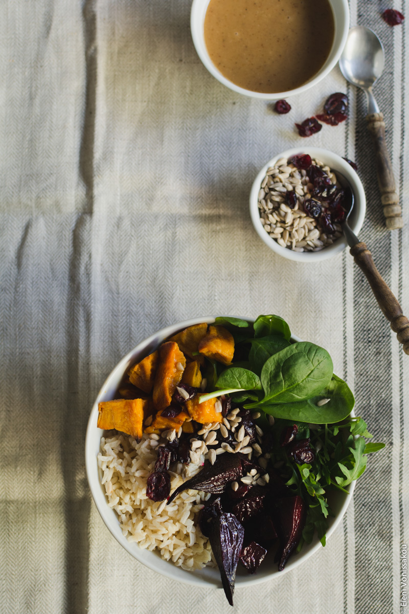 Roast Beetroot and Sweet Potato Buddha Bowl with Spicy Tahini Honey Dressing www.thefoodiecorner.gr Photo description: One bowl and its contents to the bottom of the photo. At the top right are the two small bowls of dressing and sunflower seeds with some scattered dried cranberries.