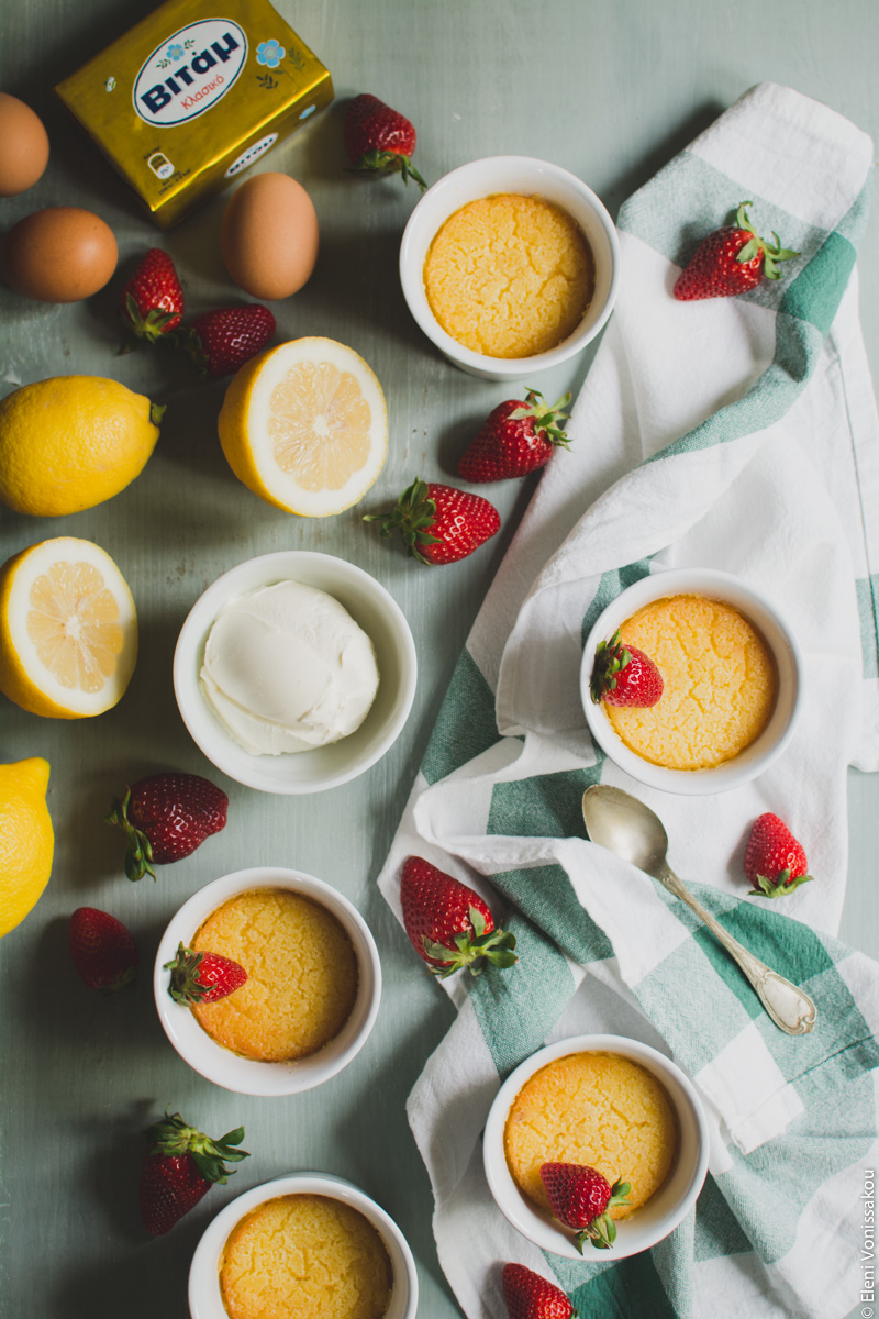 Εύκολες Πουτίγκες Λεμονιού www.thefoodiecorner.gr Photo description: The lemon puddings without the sugar on top, with just a strawberry on some of them. Set up is the same as previous. In the top left corner are some eggs and a block of Vitam margarine.