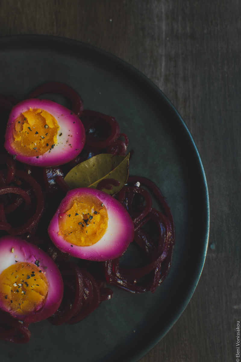 Beetroot Pickled Eggs www.thefoodiecorner.gr Photo description: A closer view of the pickled egg halves sitting on a bed of spiralized beets and onions, all turned a dark shade of pink from the beetroot juices. Some pepper flakes are visible on the egg yolks.