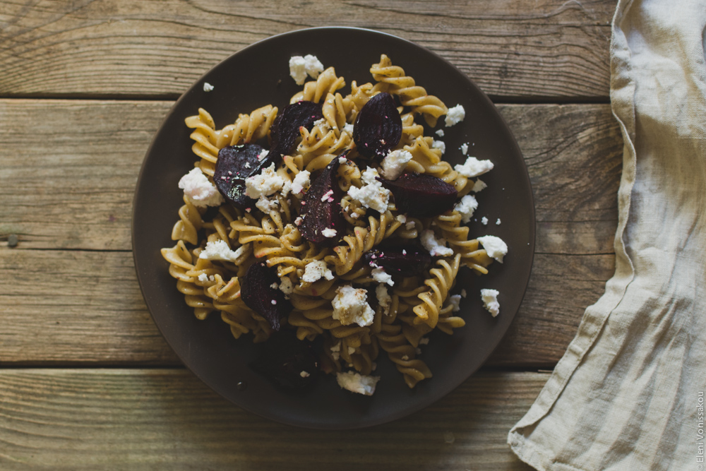 Roast Beetroot and Feta Pasta Salad with Greek Yoghurt and Cumin Dressing www.thefoodiecorner.gr Photo description: The plate of pasta salad, with fusilli shaped pasta and chunks of beetroot and crumbled feta. The plate is sitting on a wheather beaten wooden surface. To the right of the photo a beige linen napkin just visible.