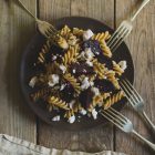 Roast Beetroot and Feta Pasta Salad with Greek Yoghurt and Cumin Dressing www.thefoodiecorner.gr Photo description: a brown plate of fusilli pasta salad on a weather beaten wooden surface. At the bottom of the photo, a linen napkin just visible. Around the plate, four forks are propped face down against the edge.