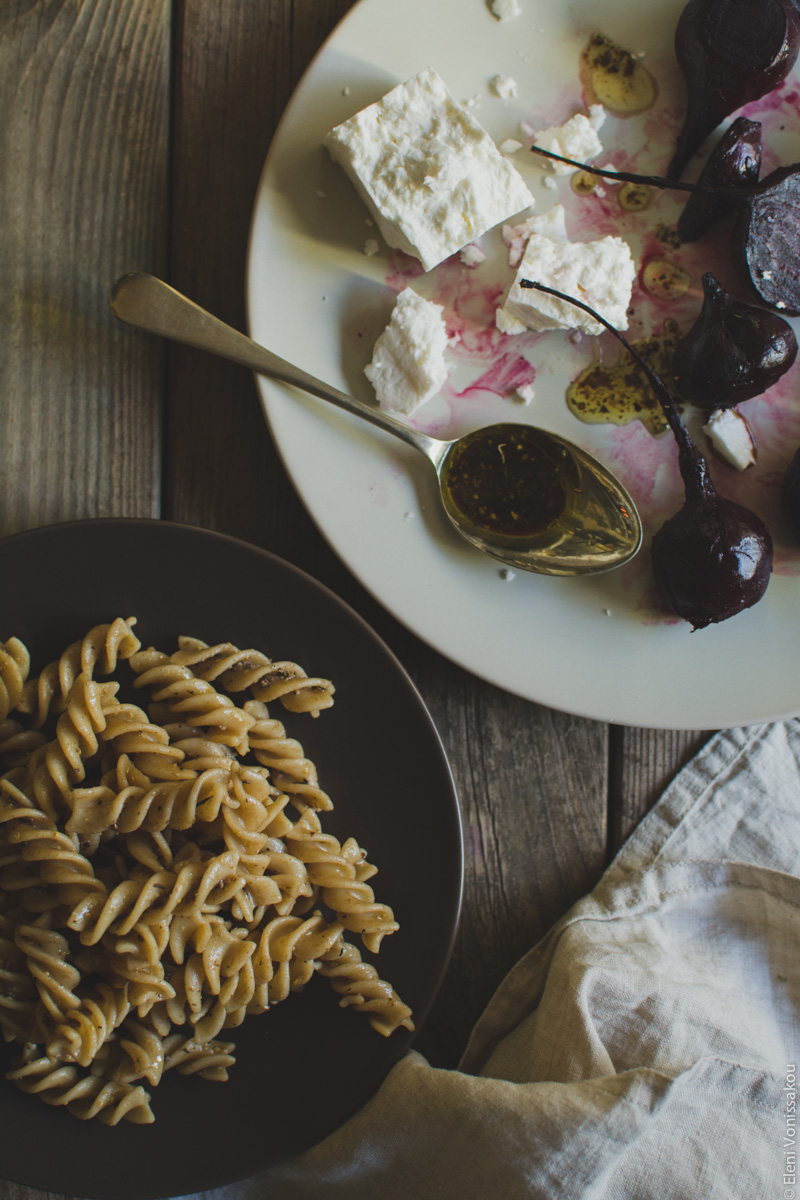 Roast Beetroot and Feta Pasta Salad with Greek Yoghurt and Cumin Dressing www.thefoodiecorner.gr Photo description: At the top right of the photo a beige plate with pieces of roasted beetroot and chunks of feta cheese. A spoon is lying on the plate with some dressing on it. To the bottom left of the photo, half visible, a plate of pasta tossed in dressing.