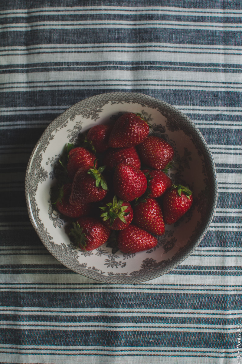 Strawberries and Cream Fridge (Icebox) Cake www.thefoodiecorner.gr Photo description: A bowl with a pretty flowery pattern around the rim, filled with whole strawberries. The bowl is in the centre of the photo, sitting on a stripy linen material.