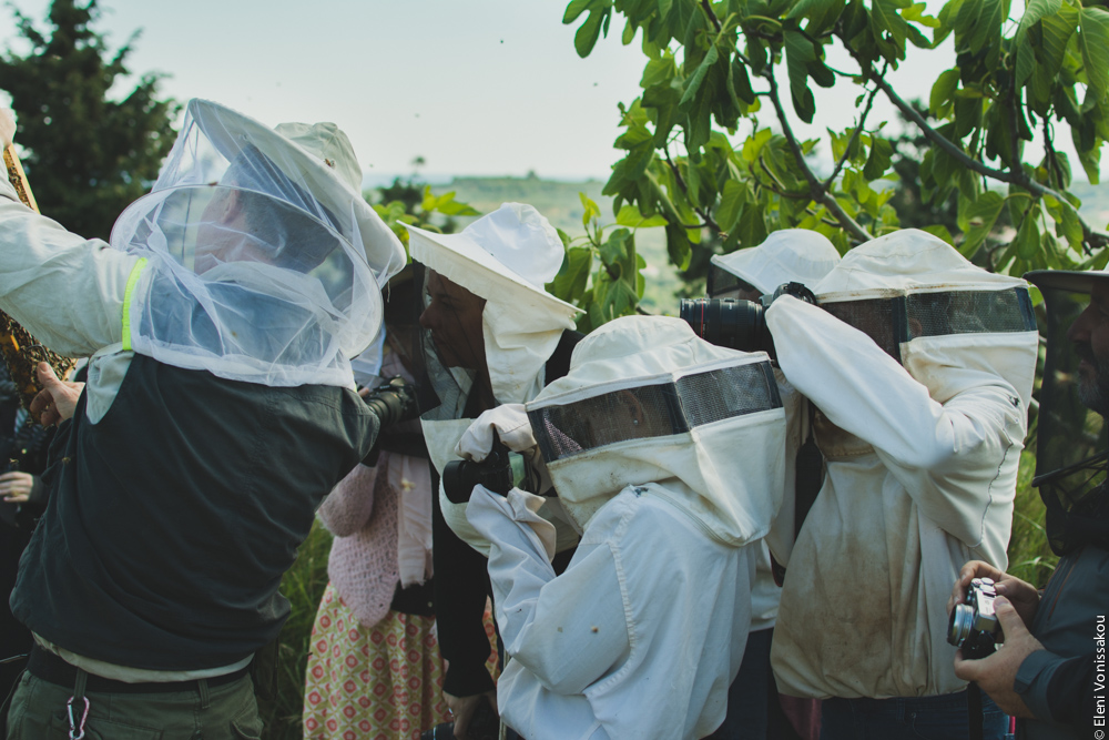 Miliaworkshop2017 www.thefoodiecorner.gr Photo description: Side view of several people in bee hive suits, all hunched together taking photos of a subject not in view.