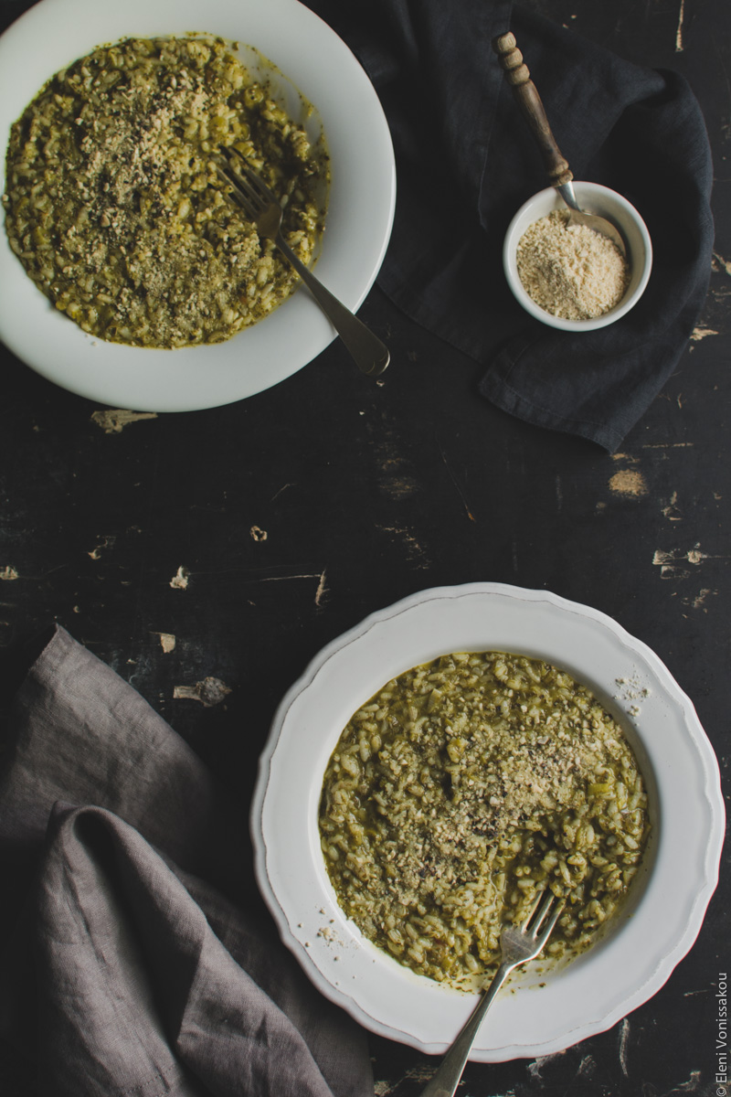 Vegan Risotto with Amaranth and Herbs www.thefoodiecorner.gr Photo description: Two plates of risotto on a dark surface, in the bottom right and top left corners of the photo. Both have forks in them, and some of the risotto is missing. To the top right is a small bowl of vegan cheese with a spoon in it. To the bottom left a bunched up gray linen napkin.