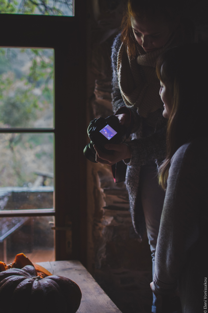 Milia Workshop 2017 – A long overdue recap. Part 1. www.thefoodiecorner.gr - Photo description: Two ladies, one of them standing on a stool, looking down at a camera screen and discussing the image on it. To the left, the subject of that image, a cut pumpkin, sitting on a wooden table. The light is coming in through a window behind the table, thus creating shadows on the ladies’ faces.