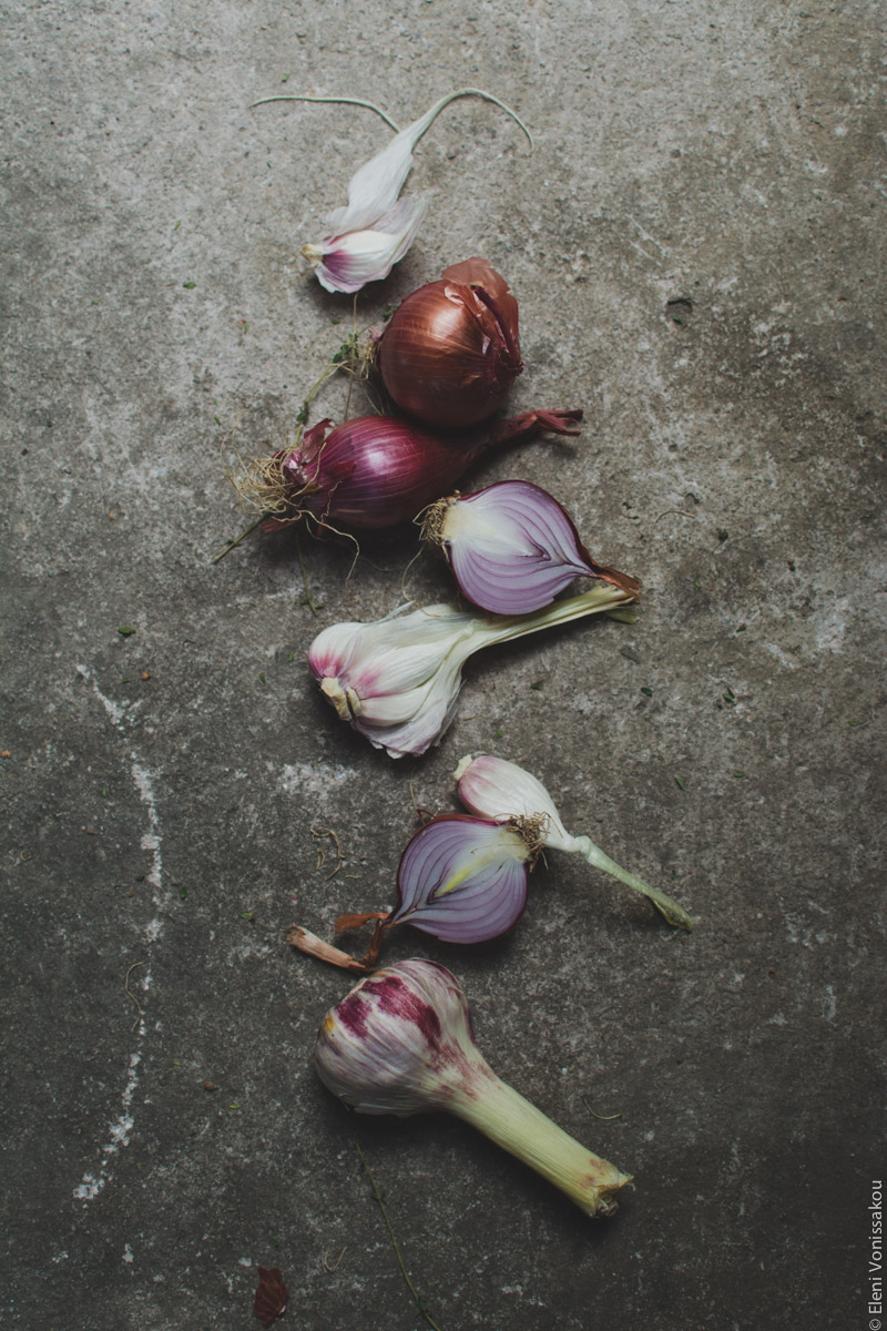 Milia Workshop 2017 – A long overdue recap. Part 1. www.thefoodiecorner.gr - Photo description: Red onions and fresh garlic laid out in a vertical line on a rough gray surface. Some of the onions are cut in half.