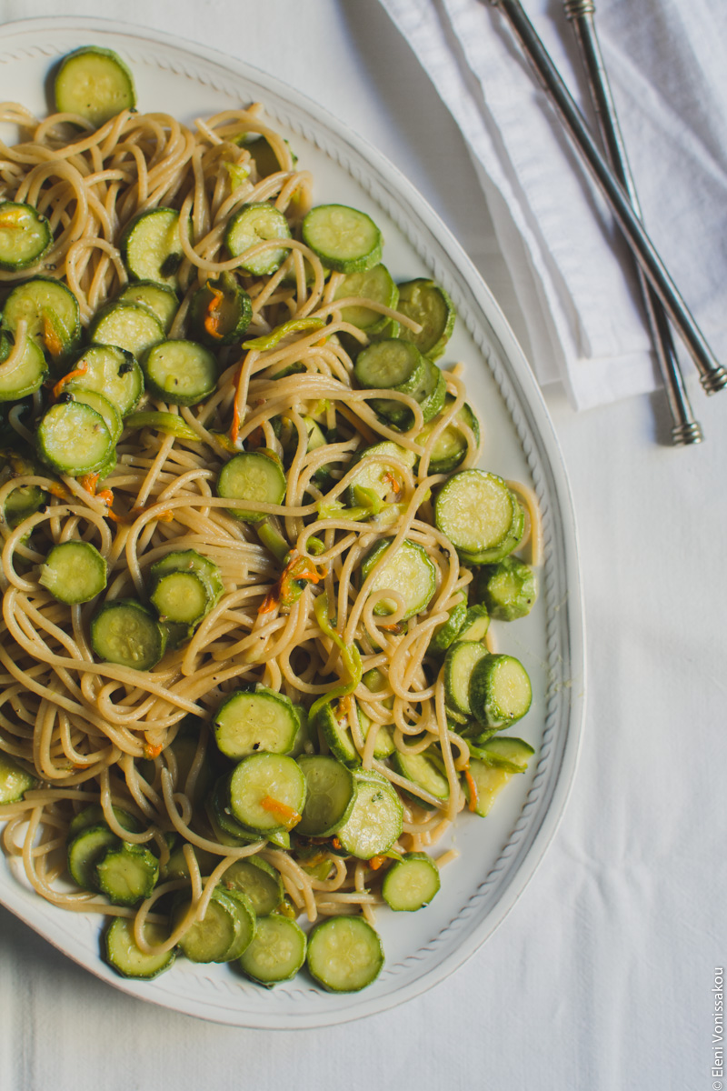 Whole Wheat Courgette Pasta with Courgette Flowers www.thefoodiecorner.gr Photo description: The platter of courgette spaghetti to the left of the photo (the right side of the platter is outside the shot). To the top right of the photo are the handles of the serving spoons lying on a linen napkin.