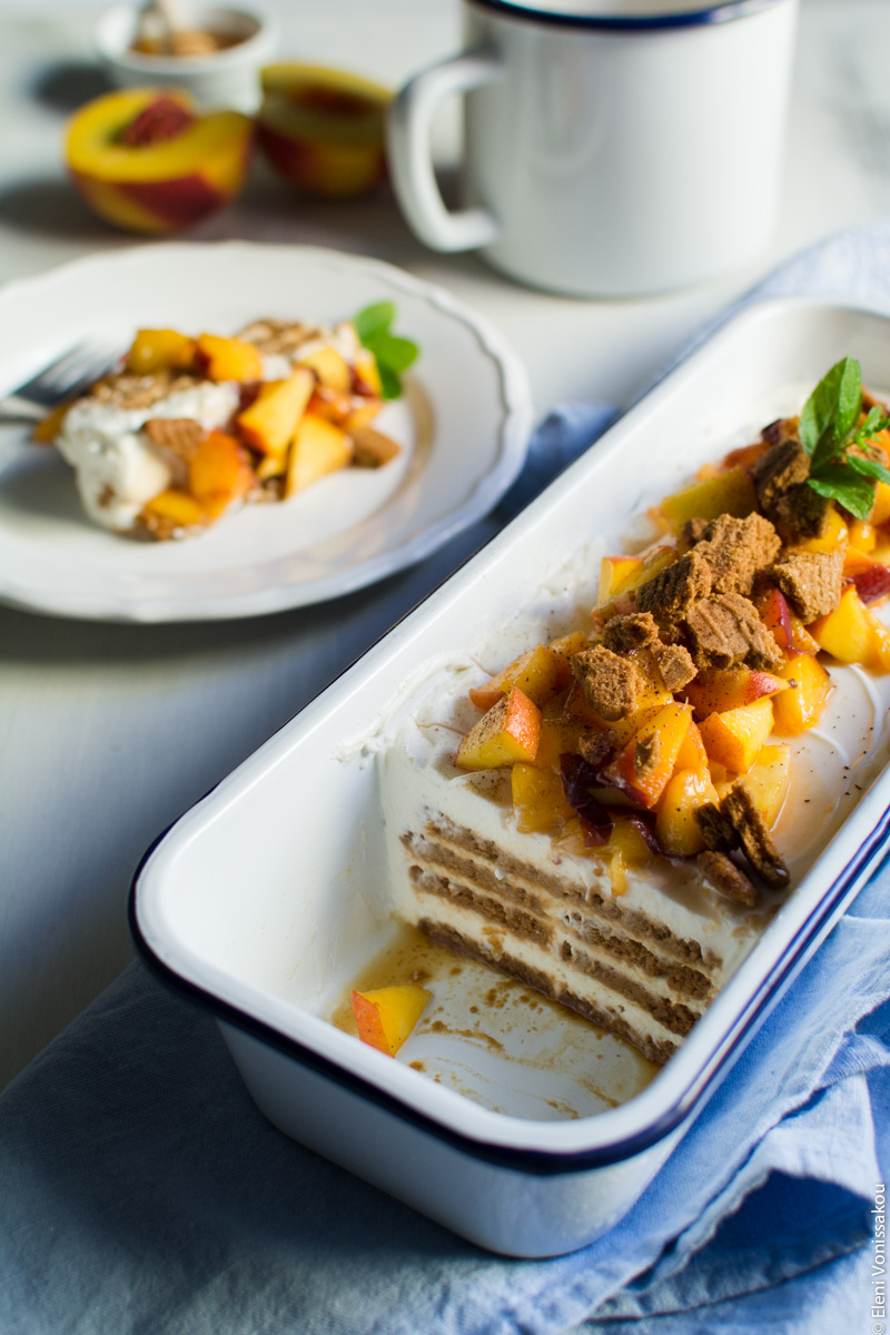 Greek Yoghurt, Mascarpone and Speculoos (Biscoff) Cookie Fridge Cake with Peaches www.thefoodiecorner.gr Photo description: A close ¾ view of the cake in the pan after some slices have been cut and removed. The layers of biscuit and cream are visible. Behind the pan a plate with a slice of cake (out of focus). Also in the background the jug, only the side of it visible.