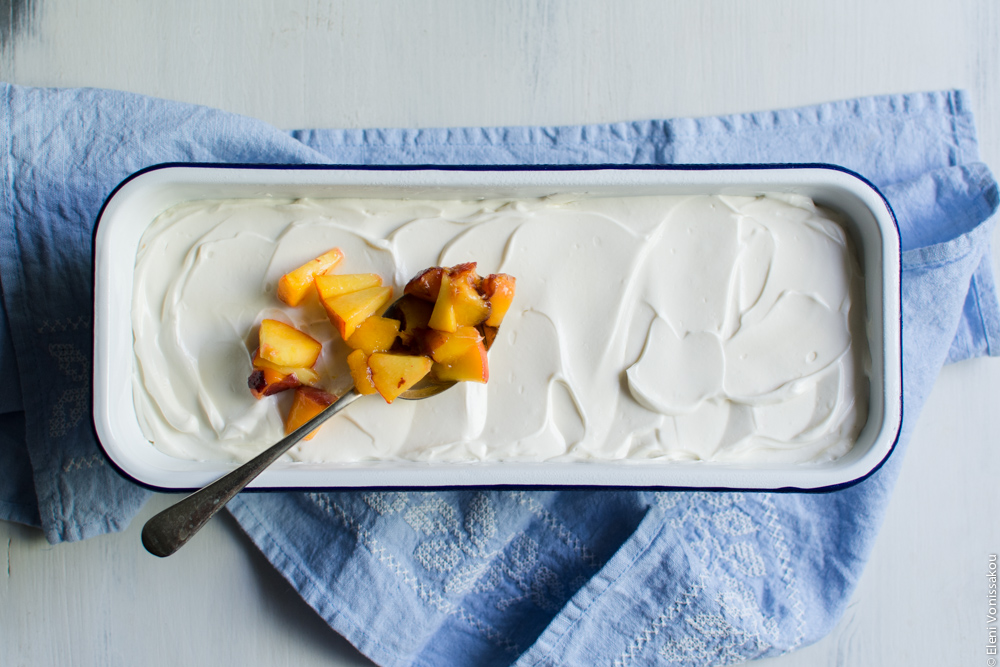 Greek Yoghurt, Mascarpone and Speculoos (Biscoff) Cookie Fridge Cake with Peaches www.thefoodiecorner.gr Photo description: Close up of just the pan with the fridge cake. A spoon with chopped peaches is sitting on top of the cake, ready to decorate it.