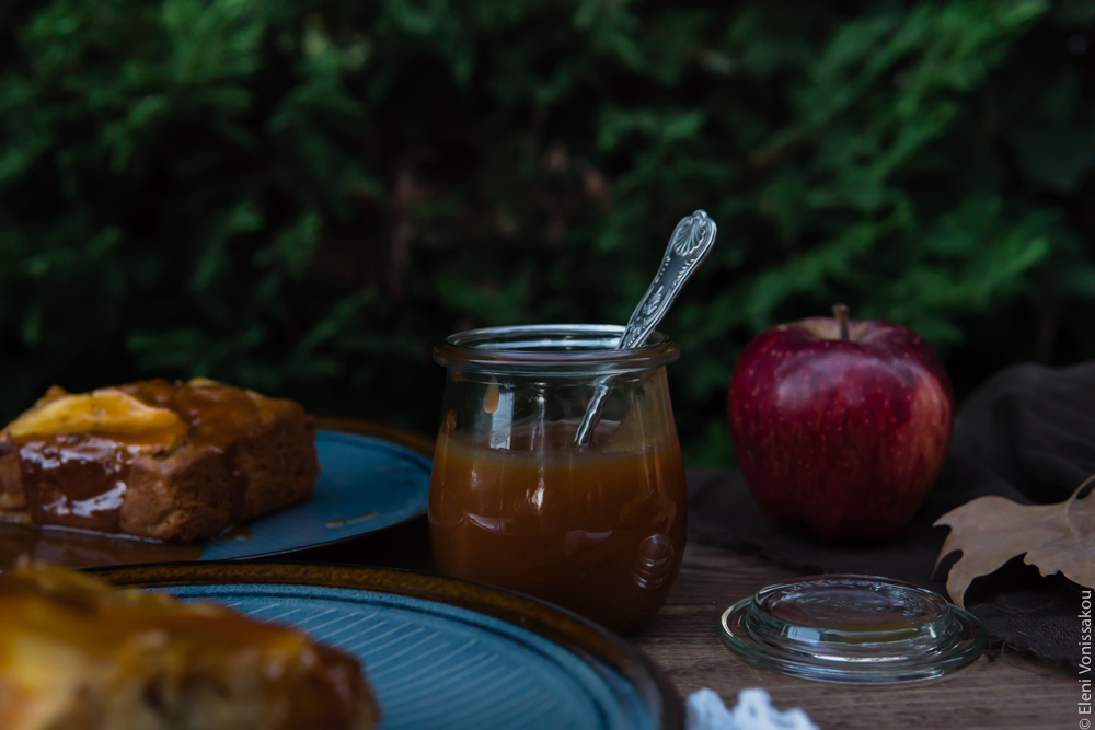 Easy, No Mixer Apple Cake with Salted Caramel Sauce www.thefoodiecorner.gr Photo description: A side view of the jar of caramel. To its right an apple and to its left a couple of plates with cake on them (half in the shot).