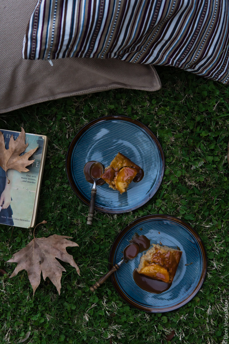 Easy, No Mixer Apple Cake with Salted Caramel Sauce www.thefoodiecorner.gr Photo description: A top view of two plates with cake on them. They are sitting on the grass, a book and some brown leaves next to them. Barely visible are two cusions.