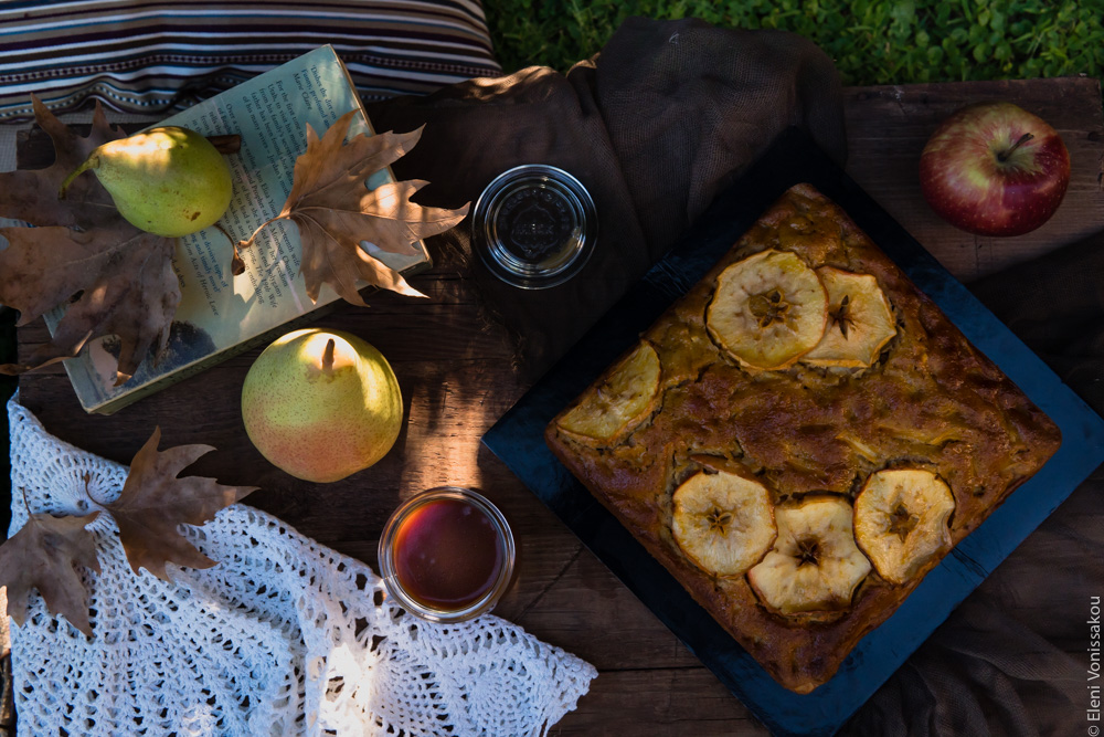 Easy, No Mixer Apple Cake with Salted Caramel Sauce www.thefoodiecorner.gr Photo description: A cake on a small table oudoors. Next to it are some apples and pears, a jar of caramel sauce, a book and some brown leaves. On one corner of the table is a small folded crocheted tablecloth.