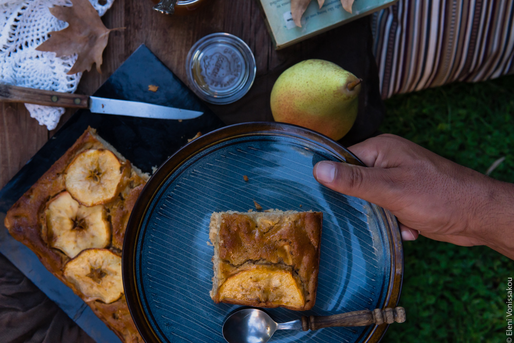 Easy, No Mixer Apple Cake with Salted Caramel Sauce www.thefoodiecorner.gr Photo description: A top view of a plate with a piece of cake being held over the table by a man’s hand.