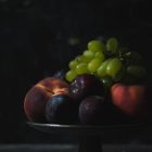 Capturing Athens Food Styling and Photography Workshop www.thefoodiecorner.gr Photo description: A cake stand with late summer fruit lying on top, peaches, plums and grapes. All against a very dark backround.