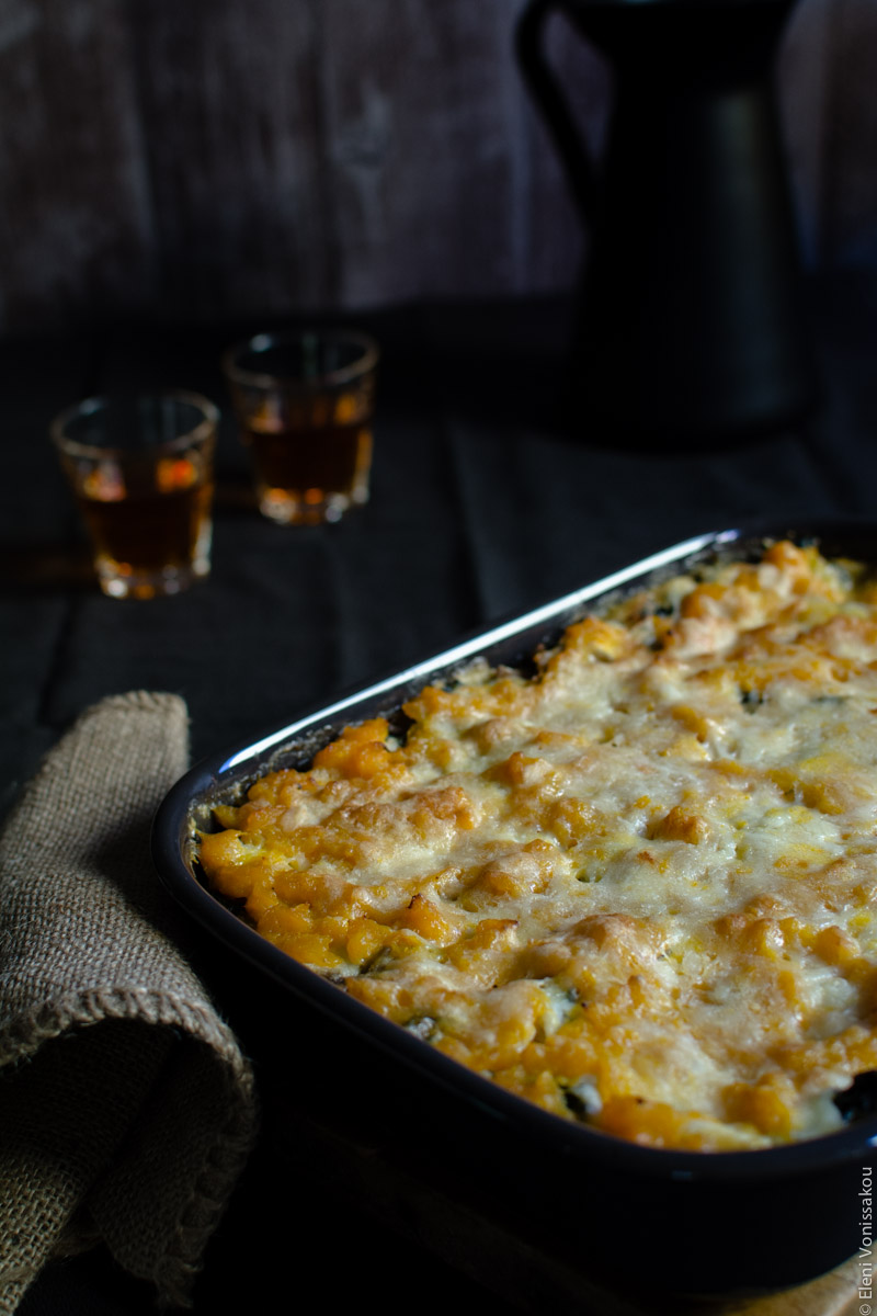 Cottage Cheese Vegetable Lasagne with Butternut Squash, Spinach and Mushrooms www.thefoodiecorner.gr Photo description: A baking dish with a cooked vegetable lasagna sitting on a dark surface. Next to it a piece of burlap acting as an oven mitt. In the background are two short glasses of wine.