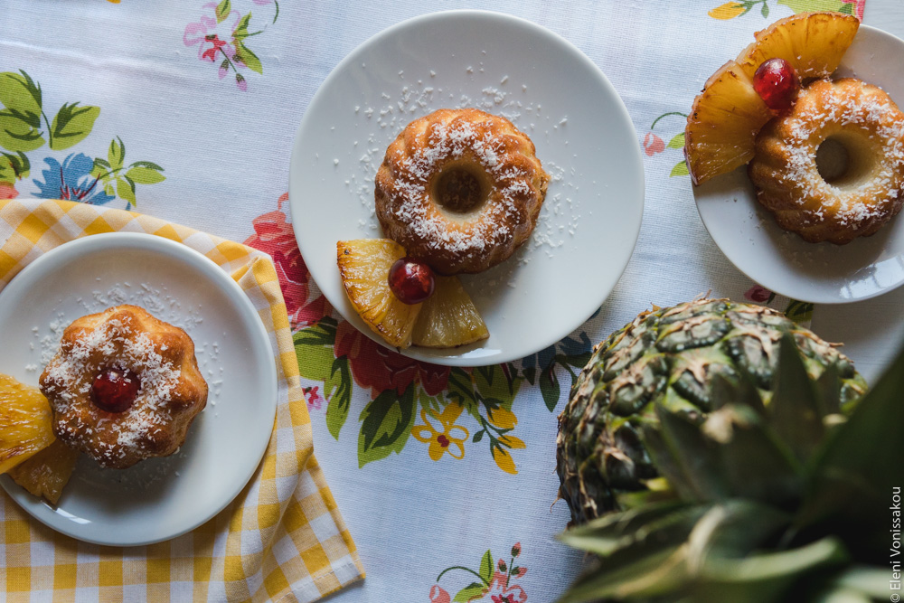 "Ραβανί" με Άρωμα Pina Colada www.thefoodiecorner.gr Photo description: Top view of three cakes on the flowery tablecloth. A pineapple is standing upright behind one of them.