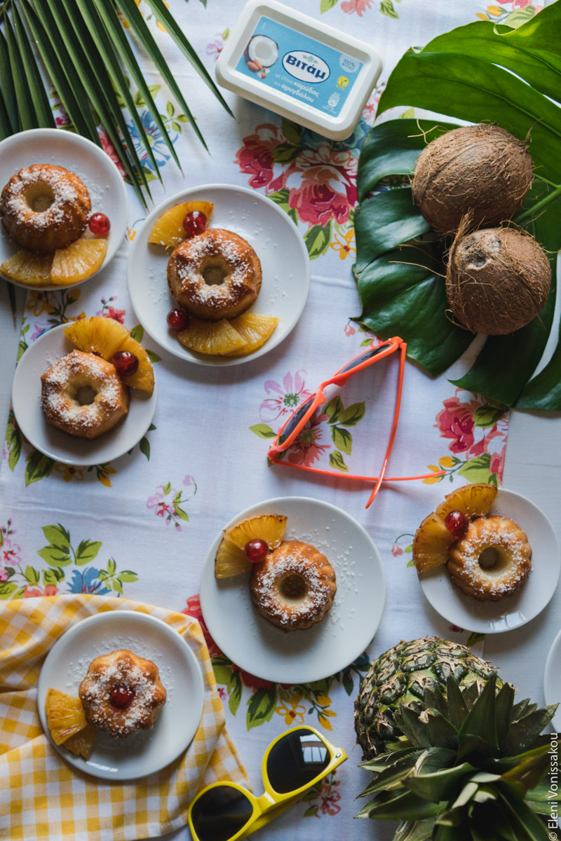 "Ραβανί" με Άρωμα Pina Colada www.thefoodiecorner.gr Photo description: All the cakes scattered around the flowery table cloth. To the top is a tub of coconut flavoured Vitam margarine. In the middle and to the bottom of the photo are two colourful pairs of sunglasses. Around the edges of the photo are some leaves, a pineapple and two coconuts.