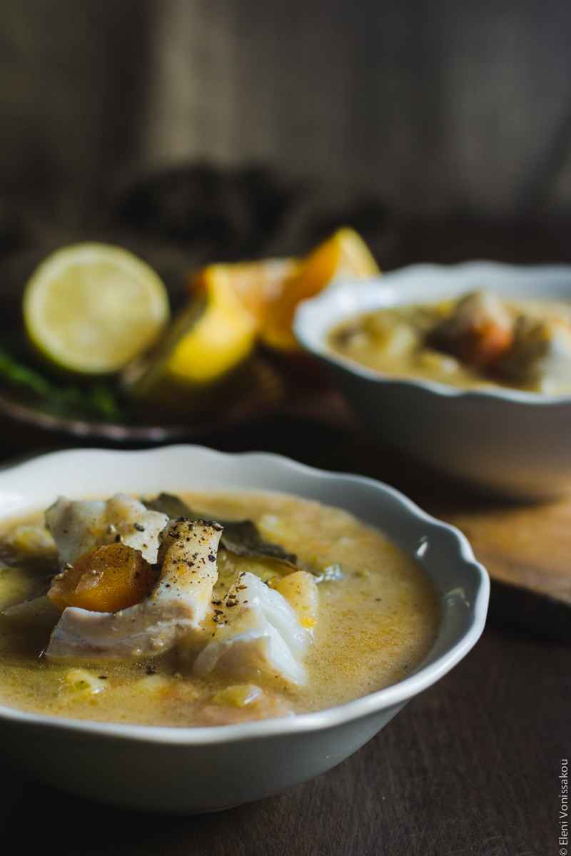 Orange and Lemon Fish Soup with Cod. My version of Greek Psarosoupa. www.thefoodiecorner.gr Photo description: A close side view of a bowl of soup and the pieces of fish and veggies which are protruding from within. Some black pepper is sprinkled on top. In the background the other bowl and some pieces of lemon and orange.