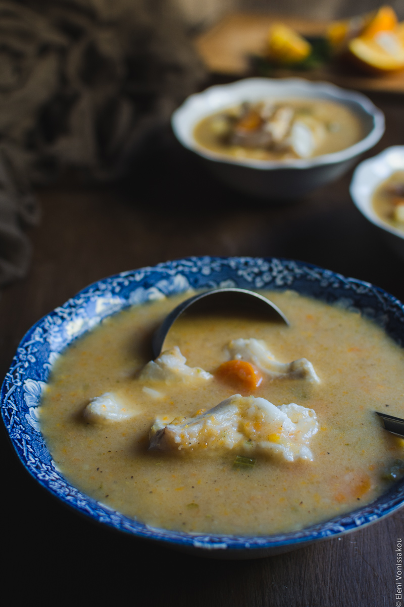 Orange and Lemon Fish Soup with Cod. My version of Greek Psarosoupa. www.thefoodiecorner.gr Photo description: A close side view of the serving bowl with the ladle inside. The soup is thick and creamy, and there are pieces of fish visible on the surface.