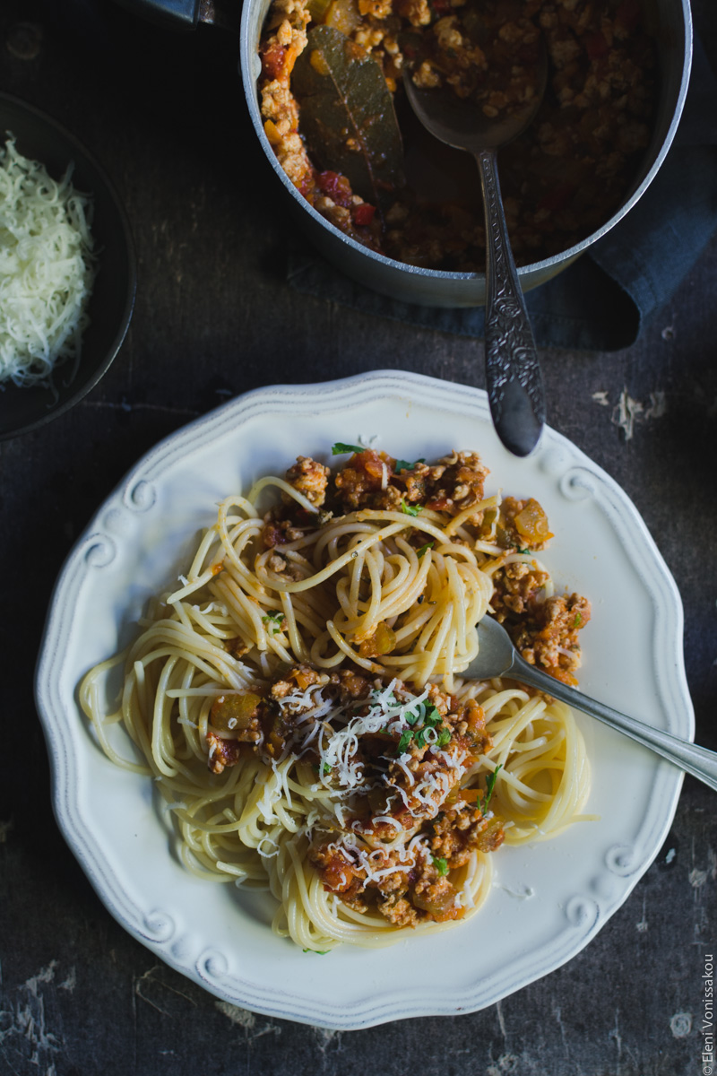 Slow Cooker Turkey Meat Sauce for Pasta (from scratch) www.thefoodiecorner.gr Photo description: A close up of a plate of spaghetti with meat sauce. The spaghetti has been mixed with a fork which is protruding from the food. To the top of the plate is a small saucepan with extra sauce in it. Barely visible to the left is a small bowl of grated cheese.