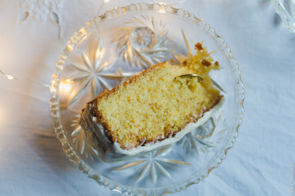 Greek New Year’s Cake (Vassilopita) with Mandarin, Almonds and Cardamom www.thefoodiecorner.gr Photo description: A slice of cake lying on a glass plate, the lucky coin protruding from the inside.