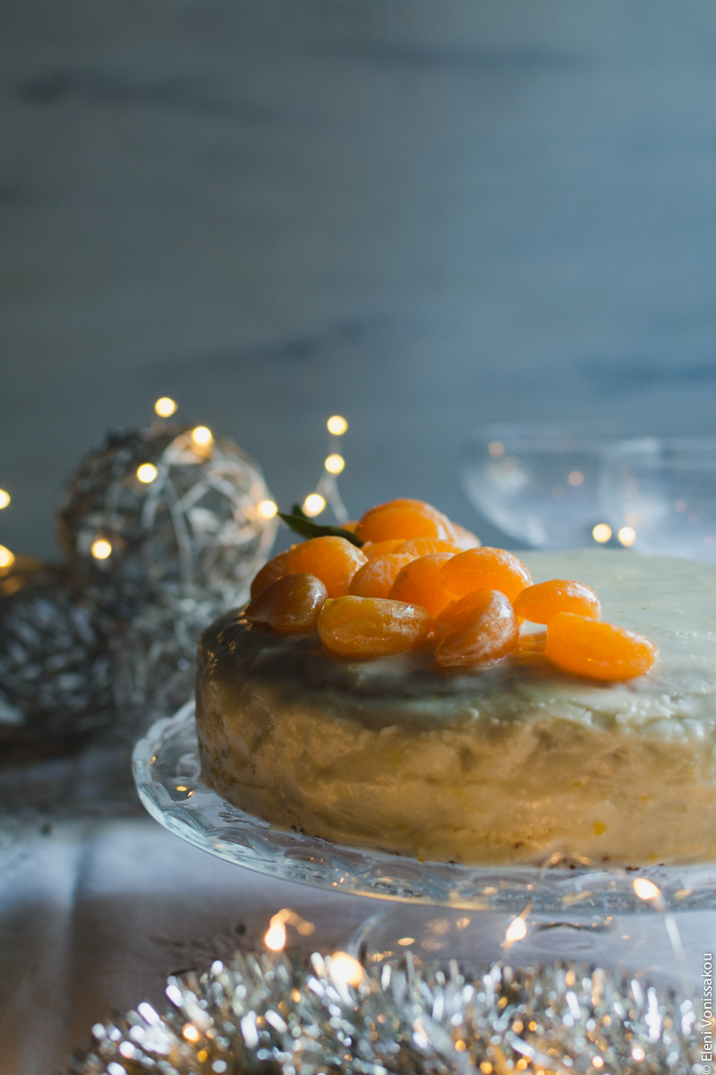 Greek New Year’s Cake (Vassilopita) with Mandarin, Almonds and Cardamom www.thefoodiecorner.gr Photo description: Side view of the cake on the stand, the light coming in from the right illuminating the mandarin segments.