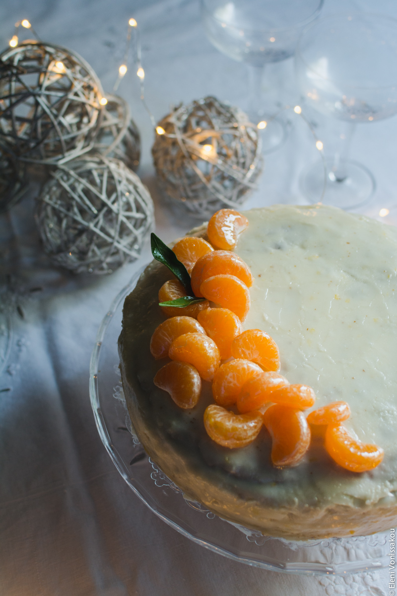 Greek New Year’s Cake (Vassilopita) with Mandarin, Almonds and Cardamom www.thefoodiecorner.gr Photo description: A ¾ view of the cake, in the background are some Christmas decorations and two champagne glasses.