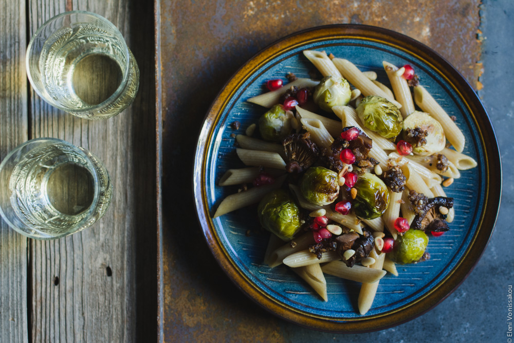 Pasta with Balsamic Roasted Brussels Sprouts and Shiitake Mushrooms (Vegan) www.thefoodiecorner.gr Photo description: A closer look at one of the plates of pasta. It is placed on a metal, rusty coloured surface. To its left on the wooden surface, two short glasses of white wine.