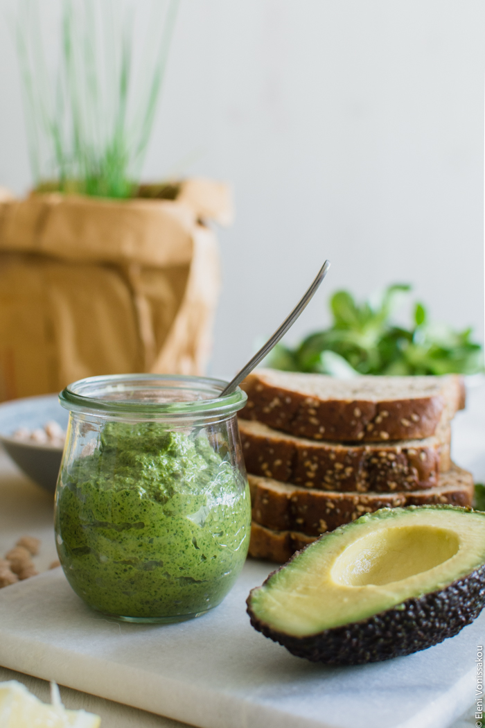 Vegan Chickpea and Tahini Sandwich with Avocado and Parsley Pesto www.thefoodiecorner.gr Photo description: A side view of a small pot of parsley pesto, sitting next to a stack of bread slices and half an avocado.