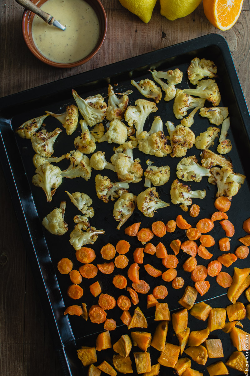 Lenten Bowls with Bulgur Wheat, Beluga Lentils, Roast Veggies and Honey Tahini Dressing www.thefoodiecorner.gr Photo description: A baking sheet with three rows of cubed roasted vegetables, cauliflower, carrots and sweet potatoes. In the top left corner a small bowl of dressing.