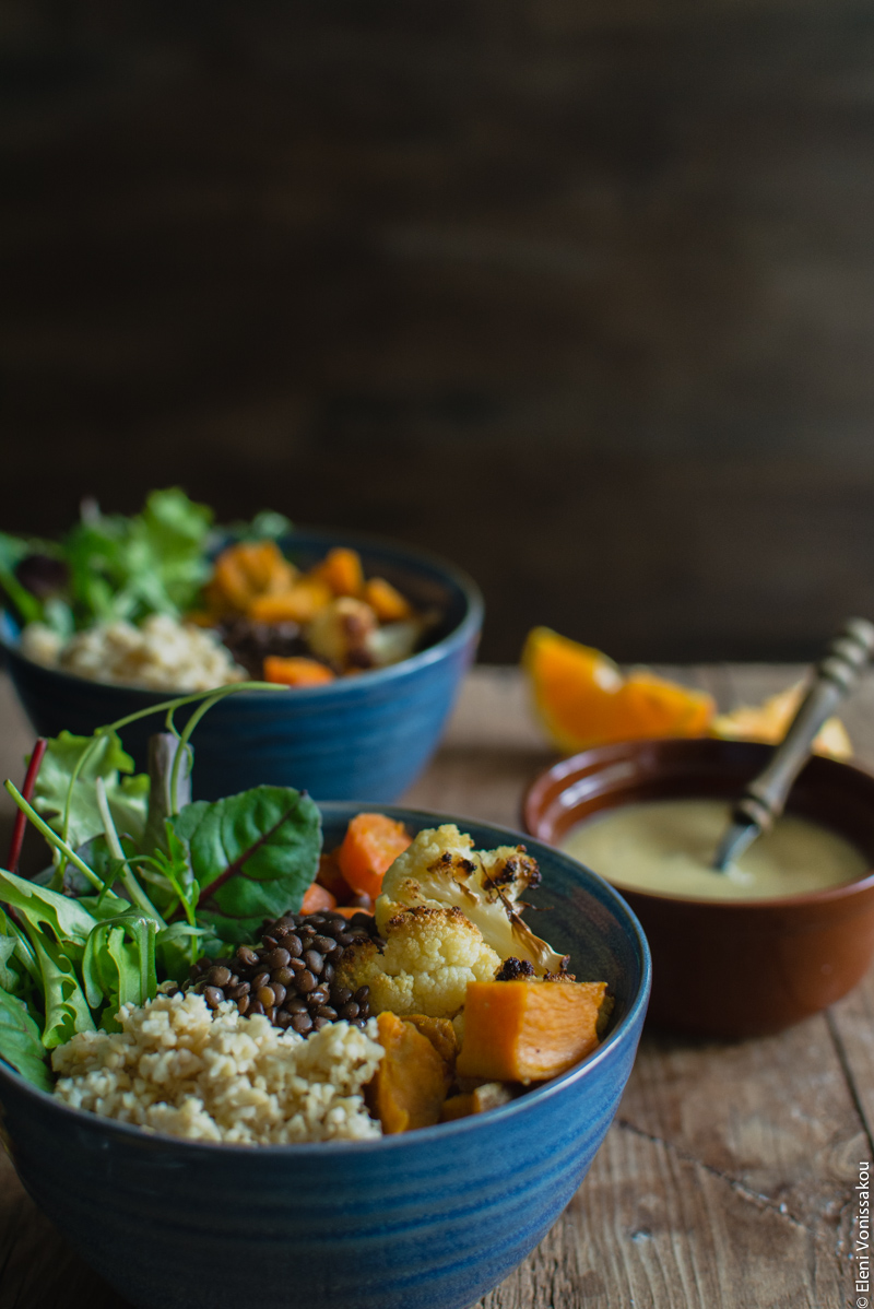 Lenten Bowls with Bulgur Wheat, Beluga Lentils, Roast Veggies and Honey Tahini Dressing www.thefoodiecorner.gr Photo description: A side view of one of the bowls against a dark background. A second bowl is barely visible behind the first, as well as a small bowl of dressing.