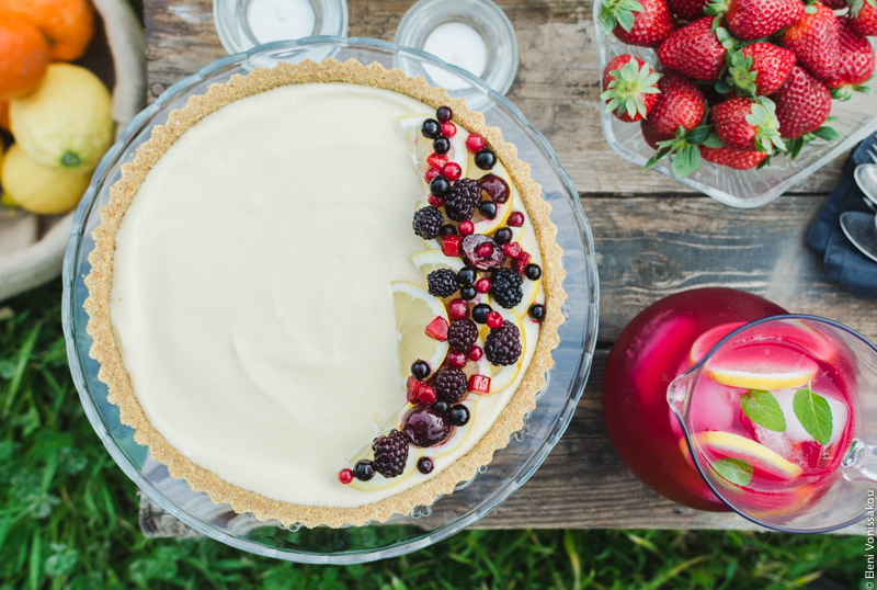 Lemon Curd and Mascarpone Cheesecake with Berries www.thefoodiecorner.gr Photo description: A closer overhead view of the cheesecake with the berries spread over the one side of its surface. To its right the jug of lemonade and the bowl of strawberries. To its left, barely visible, a basket with oranges and lemons.