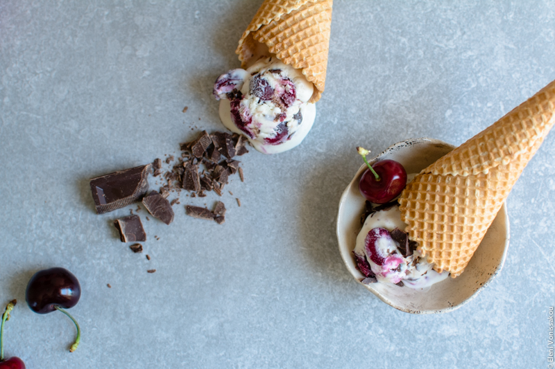 Frozen Cherry Treats – 3 Ways www.thefoodiecorner.gr Photo description: two wafer cones with ice cream, one of them half visible lying on the stone surface. The other is tipped into a small bowl. Some cherries and chopped chocolate are scattered around to the left of the photo.