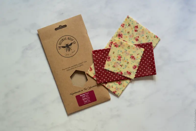 A cardboard packet and three beeswax wraps with a pretty pattern, lying on a marble surface.