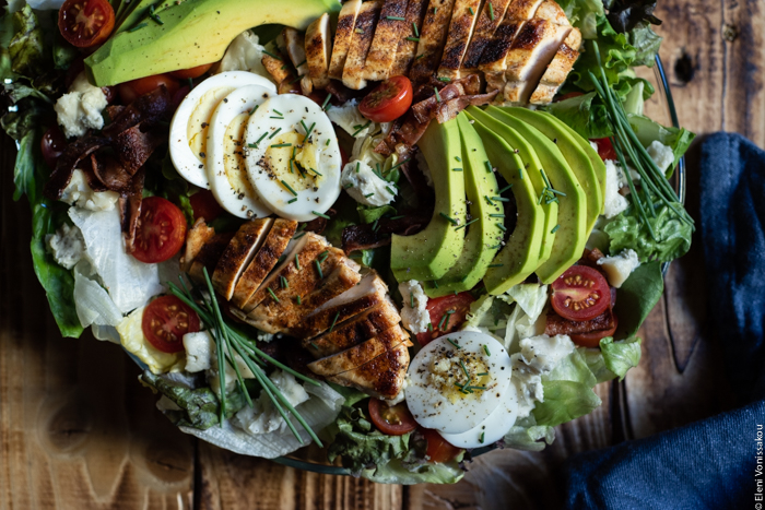 Σαλάτα Κόμπ (Cobb Salad) με Κοτόπουλο, Μπέικον και Ντρέσινγκ Γκοργκοντζόλας www.thefoodiecorner.gr Photo description: Another close up of the salad on the platter with the sliced chicken breast, avocado and egg lying on top. Cherry tomatoes are dotted here and there, and there are chopped chives sprinkled over the top.