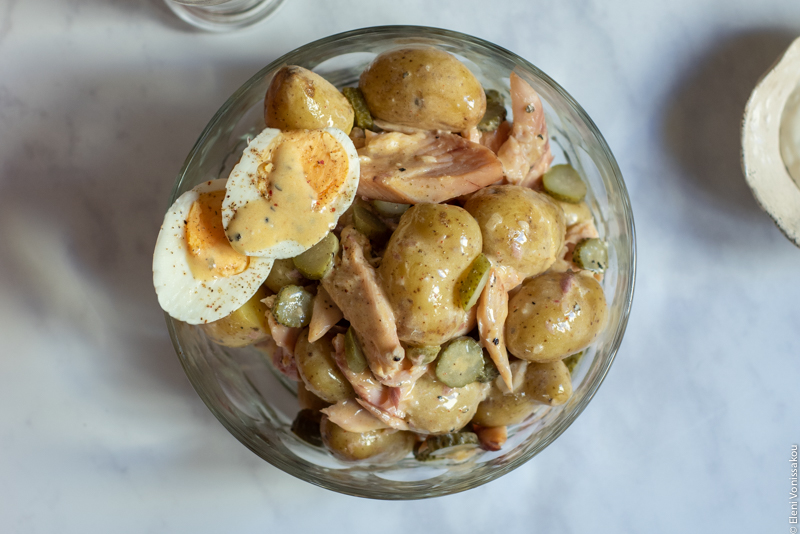 Potato Salad with Smoked Trout and a Tangy Tartare Dressing www.thefoodiecorner.gr Photo description: A close view of a salad bowl with potato salad. To one side of the salad are two halves of a boiled egg with dressing drizzled over the top.