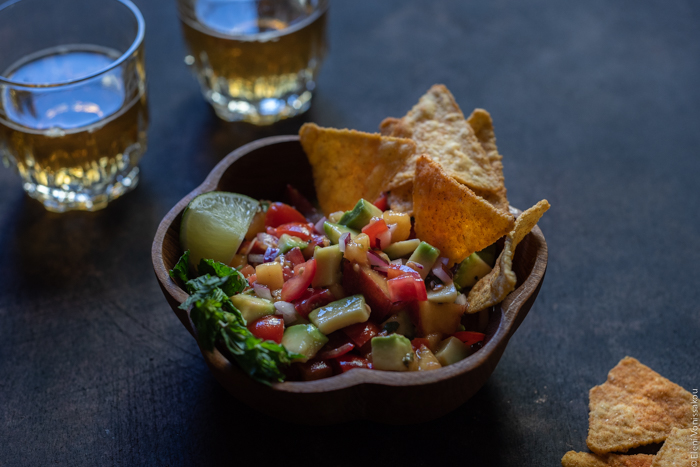 Spicy Salmon Tacos with Manouri Cheese and Peach Avocado Salsa www.thefoodiecorner.gr Photo description: A close up of the bowl of salsa, this time shot from a ¾ angle. In the bowl and at the side are some nacho chips. In the top left corner a couple of glasses of beer.