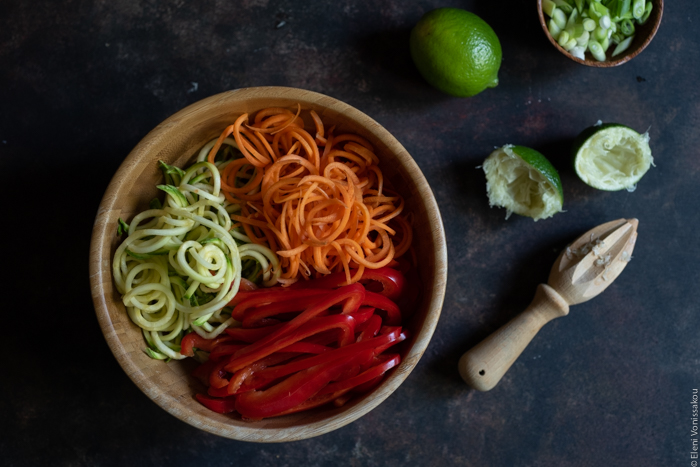 Easy Lo Mein with Salmon, Spaghetti, Veggie Noodles and Peanut Sauce www.thefoodiecorner.gr Photo description: A bowl with spiralized zucchini noodles, spiralized carrot noodles and thinly sliced red pepper. To the right of the bowl, some squeezed lime halves and a wooden juicer.