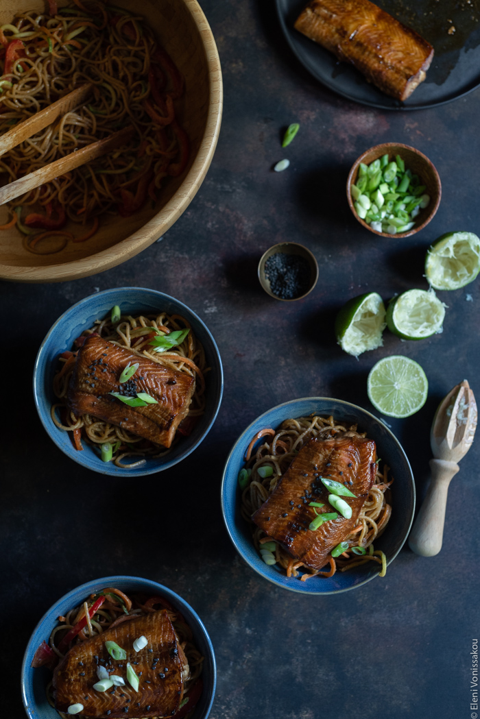 Easy Lo Mein with Salmon, Spaghetti, Veggie Noodles and Peanut Sauce www.thefoodiecorner.gr Photo description: Three bowls with noodles and salmon. At the top left the large bowl with some leftover noodles. At the top right a plate with a salmon fillet barely visible, a small bowl of chopped spring onions and some squeezed limes.