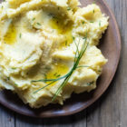 Dairy Free Garlic Mashed Potatoes with Olive Oil and a Hint of Truffle www.thefoodiecorner.gr Photo description: A close view of mashed potatoes on a ceramic plate. The top is uneven, with pools of olive oil here and there, and a small bunch of chives arranged at the side.