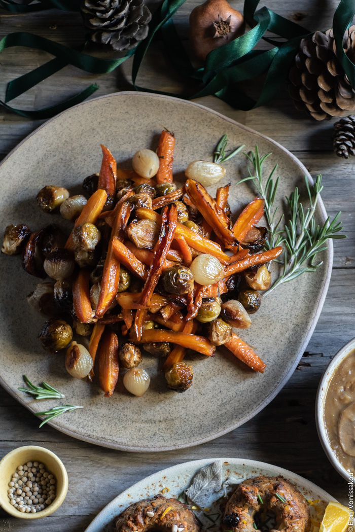 Balsamic Maple Roasted Carrots, Brussels Sprouts and Shallots (Vegan) www.thefoodiecorner.gr Photo description: A top view of the ceramic plate with the roasted veggies, some of them blackened from the oven. Around them, not quite visible, some more plates, pine cones and ribbon.