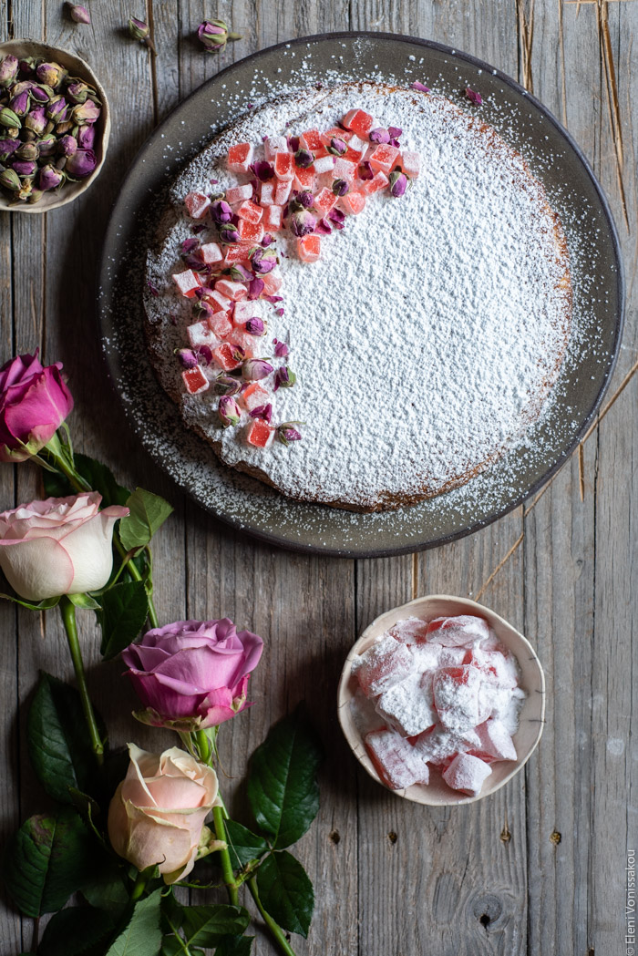 Almond Cardamom Rose Cake with Semolina and Olive Oil www.thefoodiecorner.gr Photo description: the cake in the top part of the photo. To the bottom are some roses and a small bowl of turkish delight.